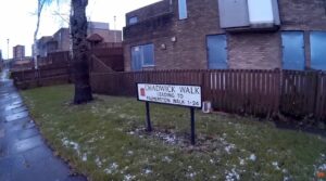 An image showing a street sign and boarded up buildings.